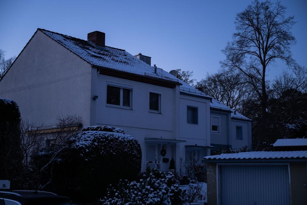 Vier Reihenhäuser in Berlin. In allen Häusern ist das Licht aus, weil der Strom ausgefallen ist. Abenddämmerung hat eingesetzt. Die Natur ist winterlich, Büsche mit Schnee bedeckt.