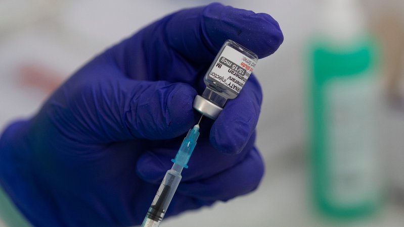 Blauer Handschuh mit Spritze und Ampulle mit an BA.1 angepasstem Covid-19-Impfstoff