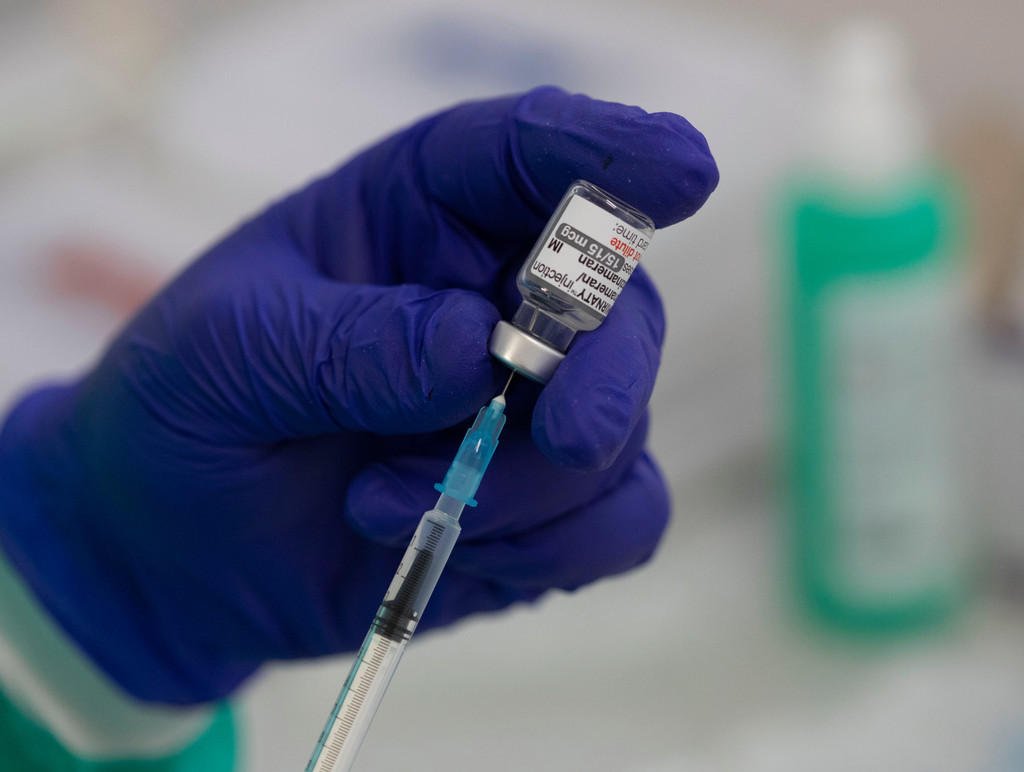 Blauer Handschuh mit Spritze und Ampulle mit an BA.1 angepasstem Covid-19-Impfstoff
