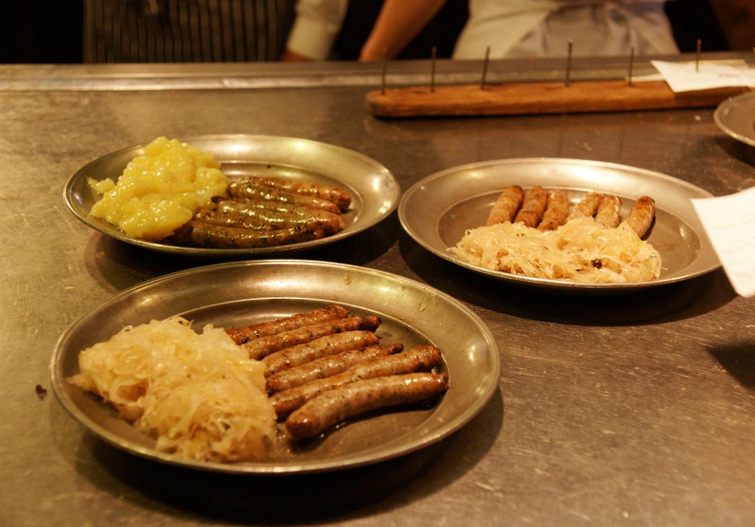 Drei Teller mit Nürnberger Rostbratwürsten und Beilagen stehen auf einem Tisch.