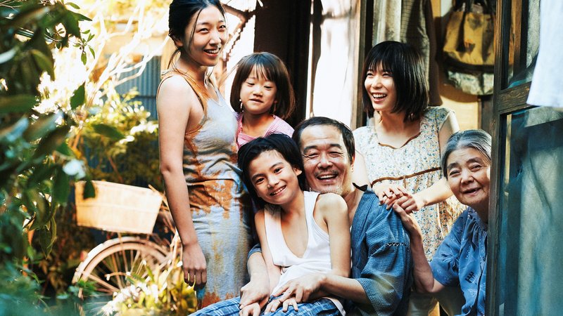 Eine lachende japanische Familievor ihrer Hütte: Szene aus "Shoplifters - Familienbande"