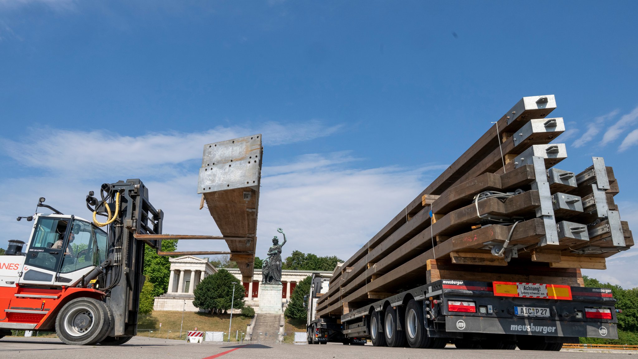Riesige Zeltbalken werden morgens auf der Theresienwiese mit einem Gabelstapler zum Aufbau von einem Lastwagen abgeladen. Im Hintergrund ist die Bavaria zu sehen.