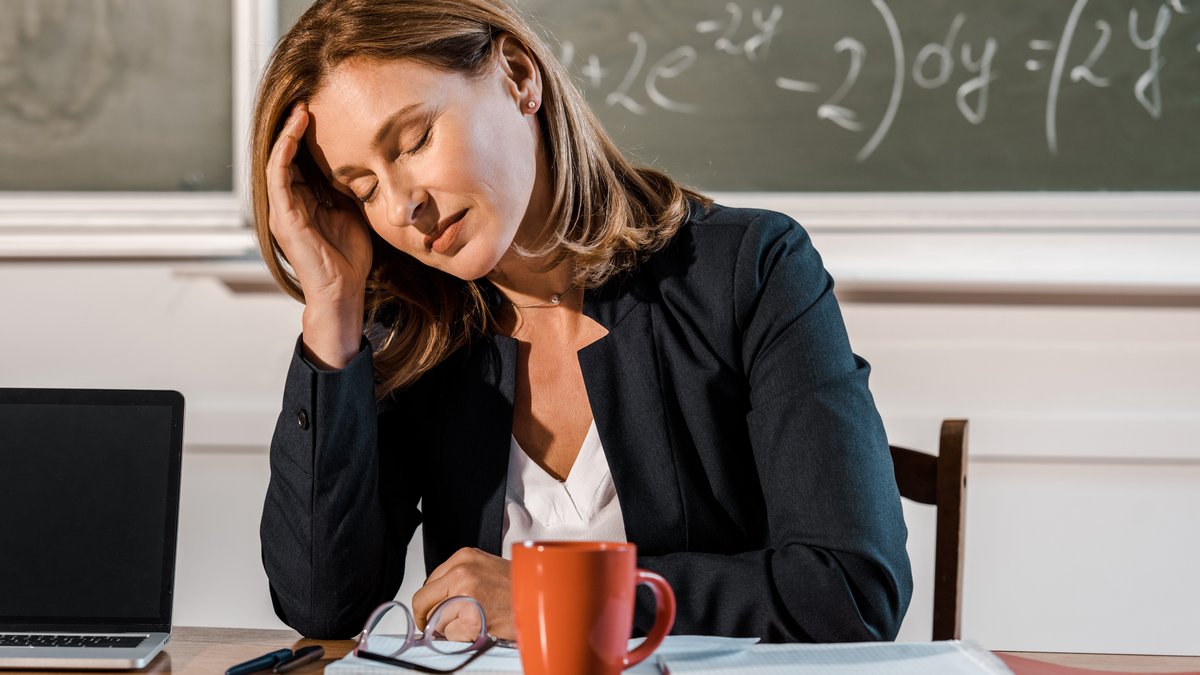 Eine Lehrerin sitzt erschöpft am Tisch ihres Klassenzimmers