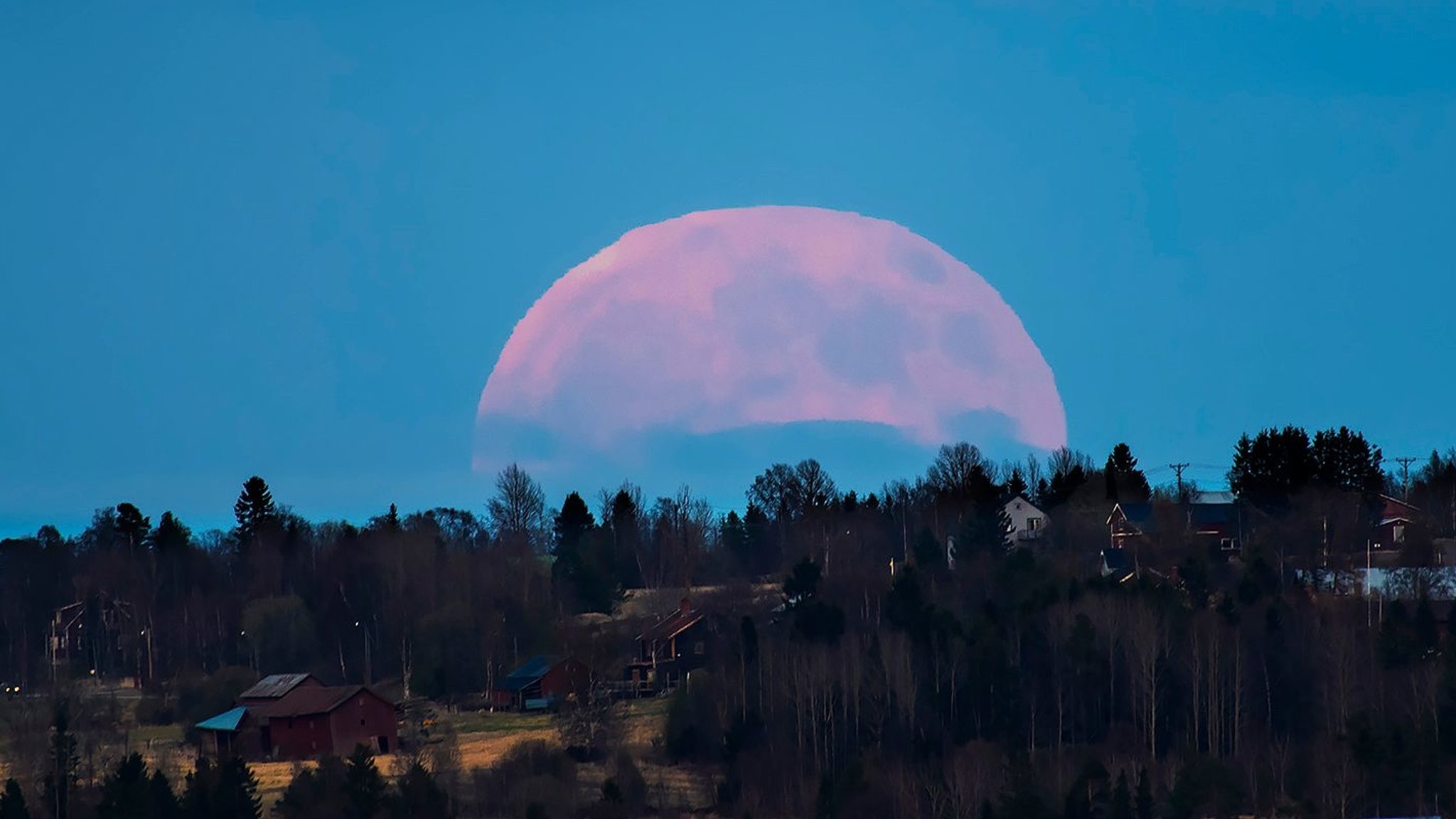 Bei geeigneter Perspektive, z. B. Häusern oder Straßen im Vordergrund, sieht der Vollmond am Horizont größer aus als normal.