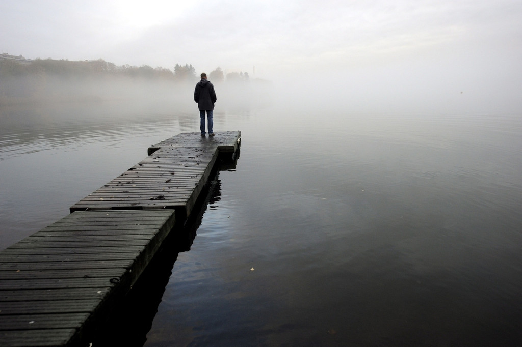 Ein Mann steht auf einem Steg am See bei nebeligen. trüben Wetter.