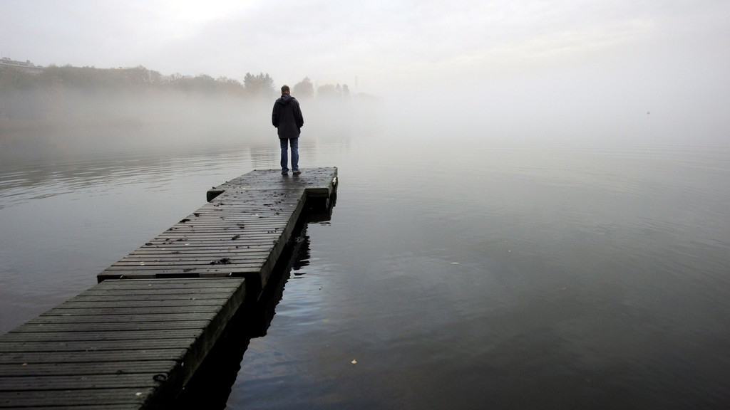 Ein Mann steht auf einem Steg am See bei nebeligen. trüben Wetter.