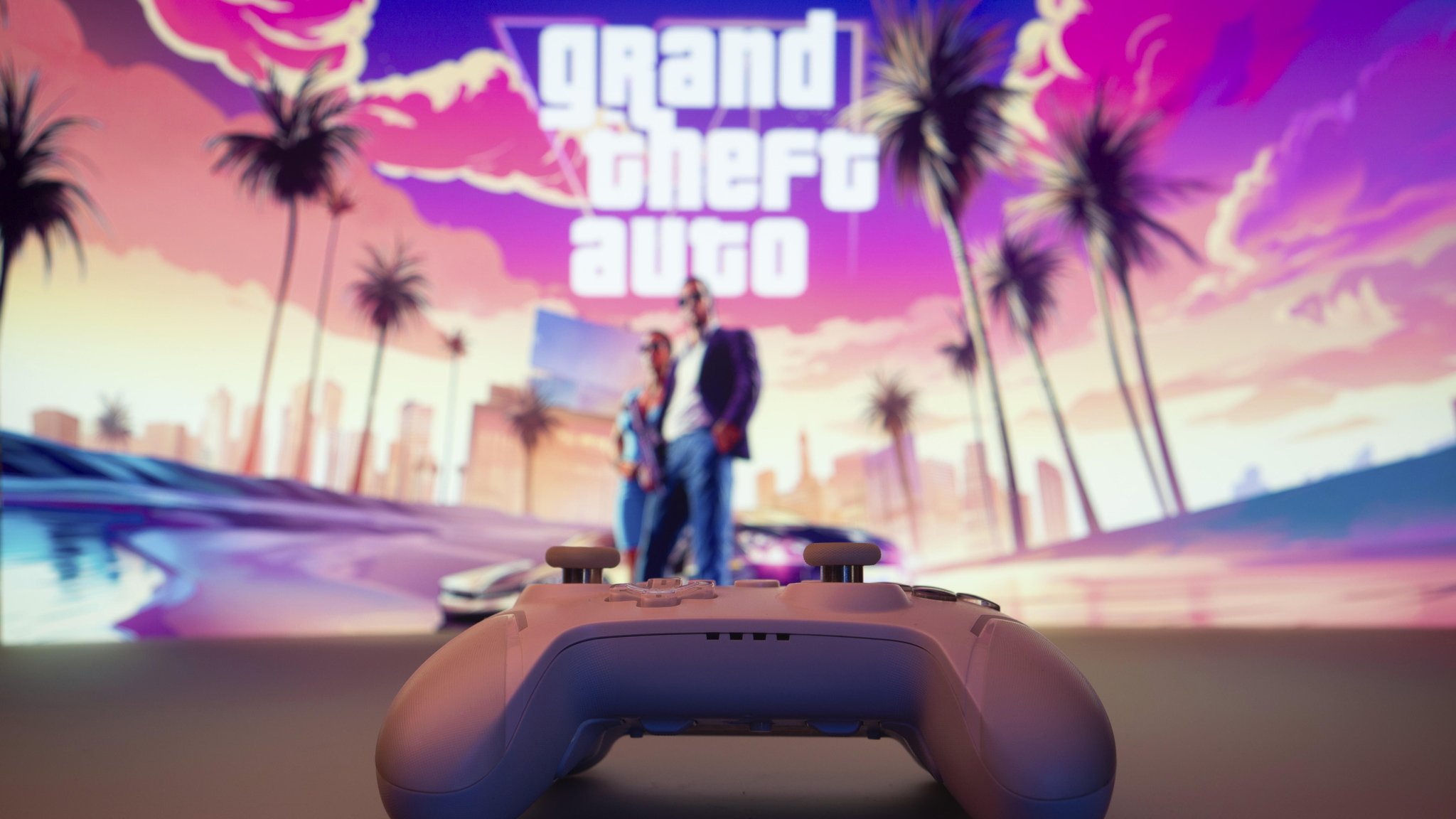 Eine Nahaufnahme eines weißen Gamepads mit Grand Theft Auto VI auf dem Bildschirm im Hintergrund. 