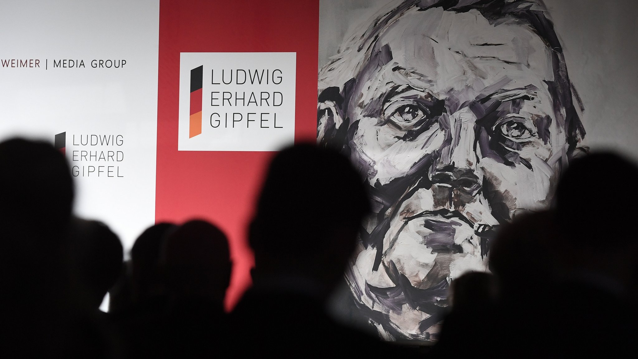 (Archivbild): Eine Zeichnung des ehemaligen Bundeskanzlers Ludwig-Erhard ist zwischen Gästen beim Ludwig-Erhard-Gipfel zu sehen. | Bild: pa/dpa/Angelika Warmuth (Archivbild): Eine Zeichnung des ehemaligen Bundeskanzlers Ludwig-Erhard ist zwischen Gästen beim Ludwig-Erhard-Gipfel zu sehen.