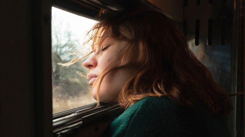Frau lässt sich am Zugfenster den Wind um die Nase wehen.