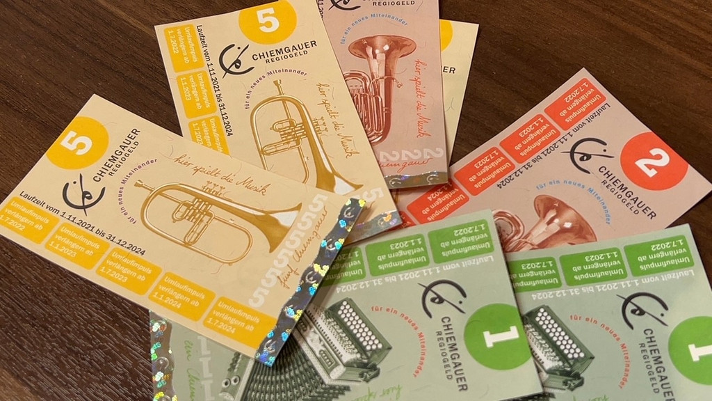 "Chiemgauer" Geldscheine in verschiedenen Farben (gelb, grün, rot) und mit verschiedenen Instrumenten darauf liegen auf einem Tisch