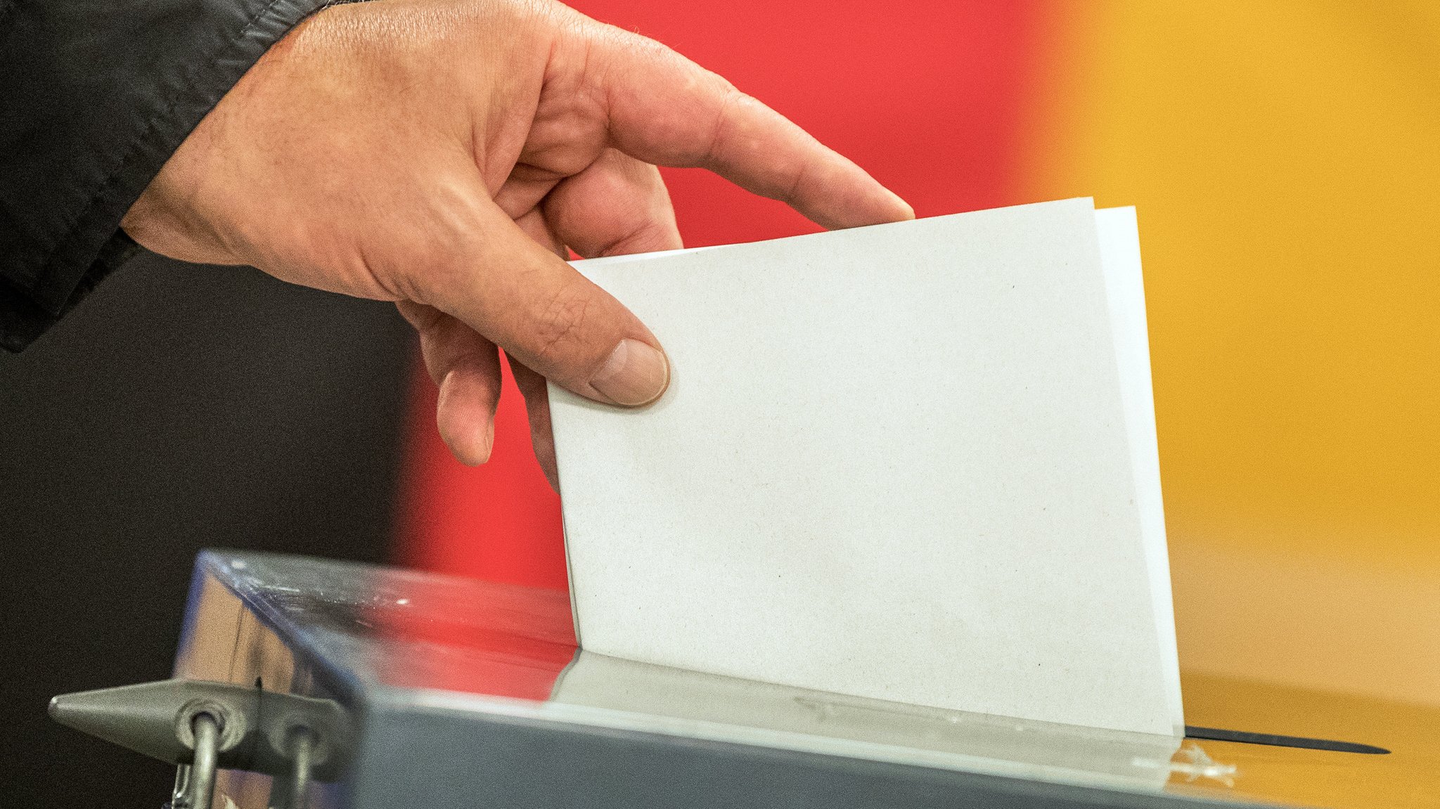 Ein Hand wirft einen Zettel in eine Wahlurne