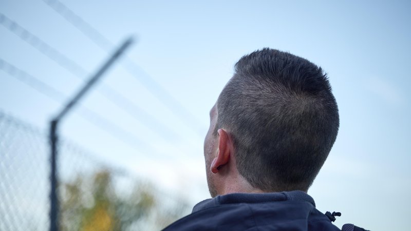 Mann steht vor hohem Stacheldrahtzaun | Bild: picture alliance / CHROMORANGE | Michael Bihlmayer Mann steht vor hohem Stacheldrahtzaun