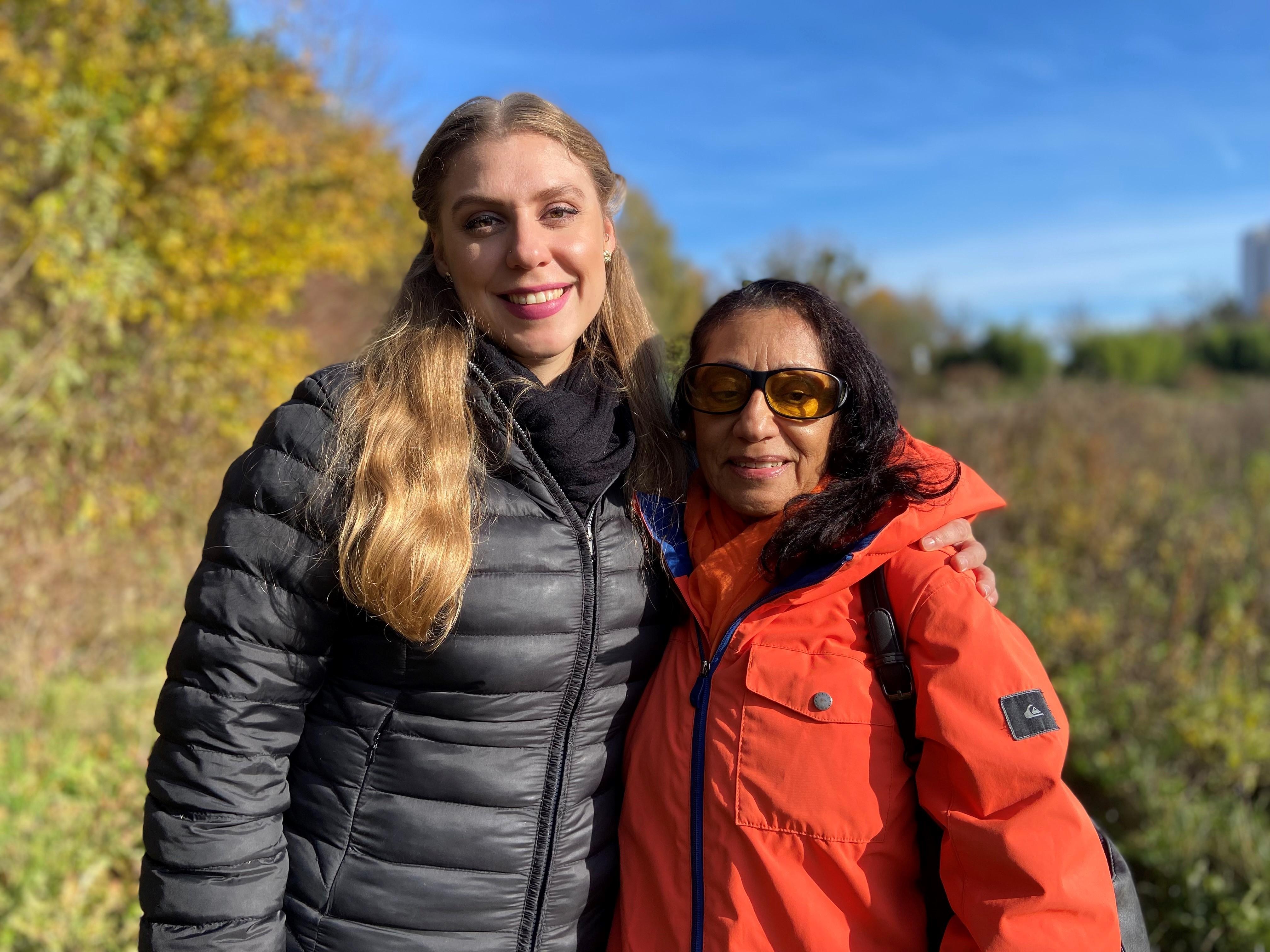 Britta, eine 37-Jährige, steht neben ihrer Mutter auf einem Feld. Sie lächeln in die Kamera.