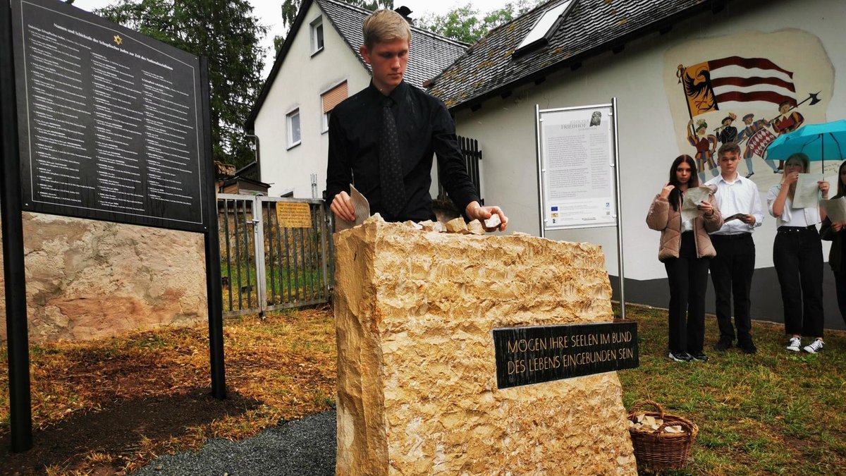 Ein schwarz gekleideter Schüler legt einen Stein auf einen Gedenkstein für die Opfer der Schoa in Schopfloch.