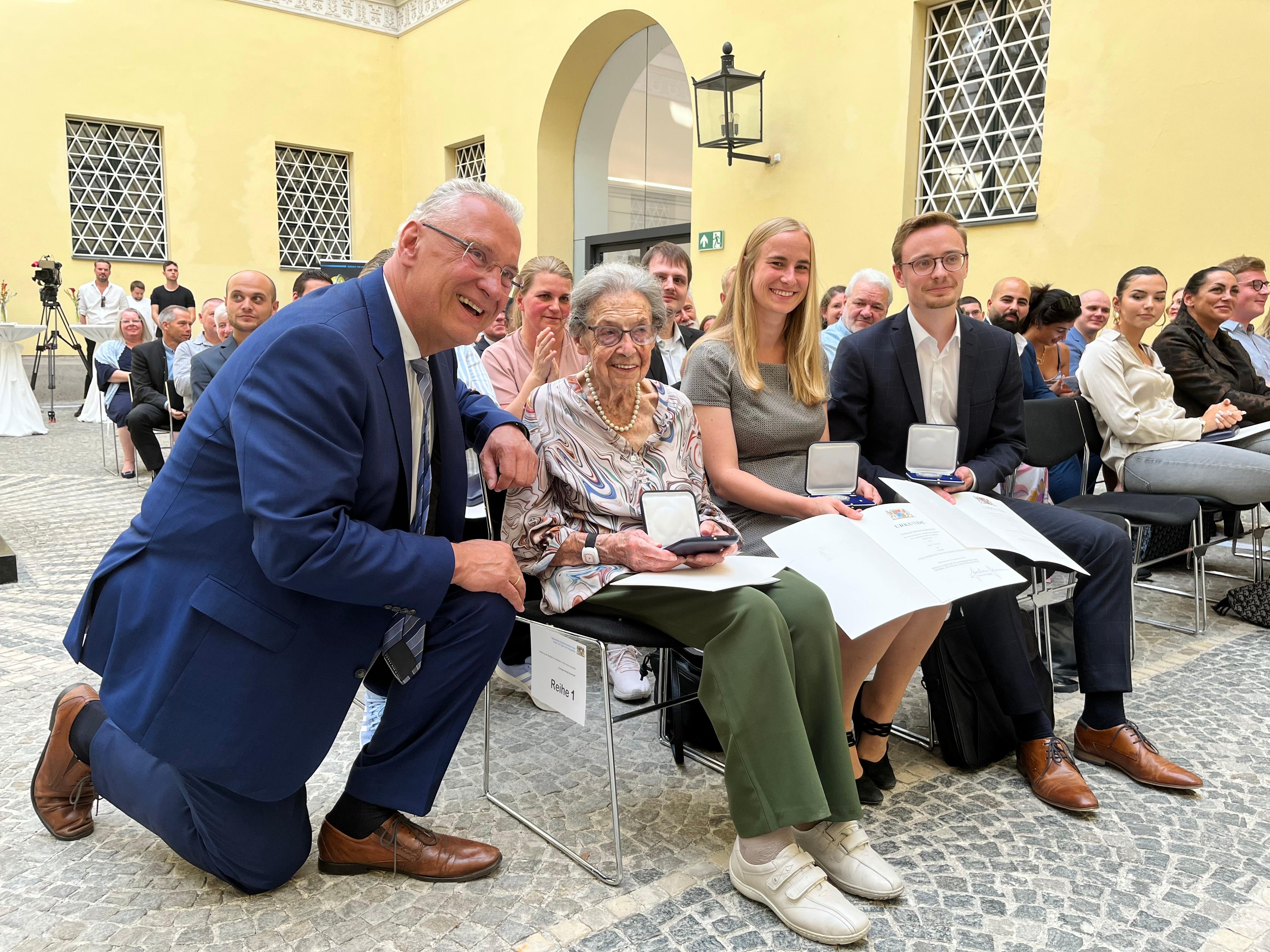 Innenminister Herrmann kniet neben Margareta Fischer und ihren jungen Nachbarn