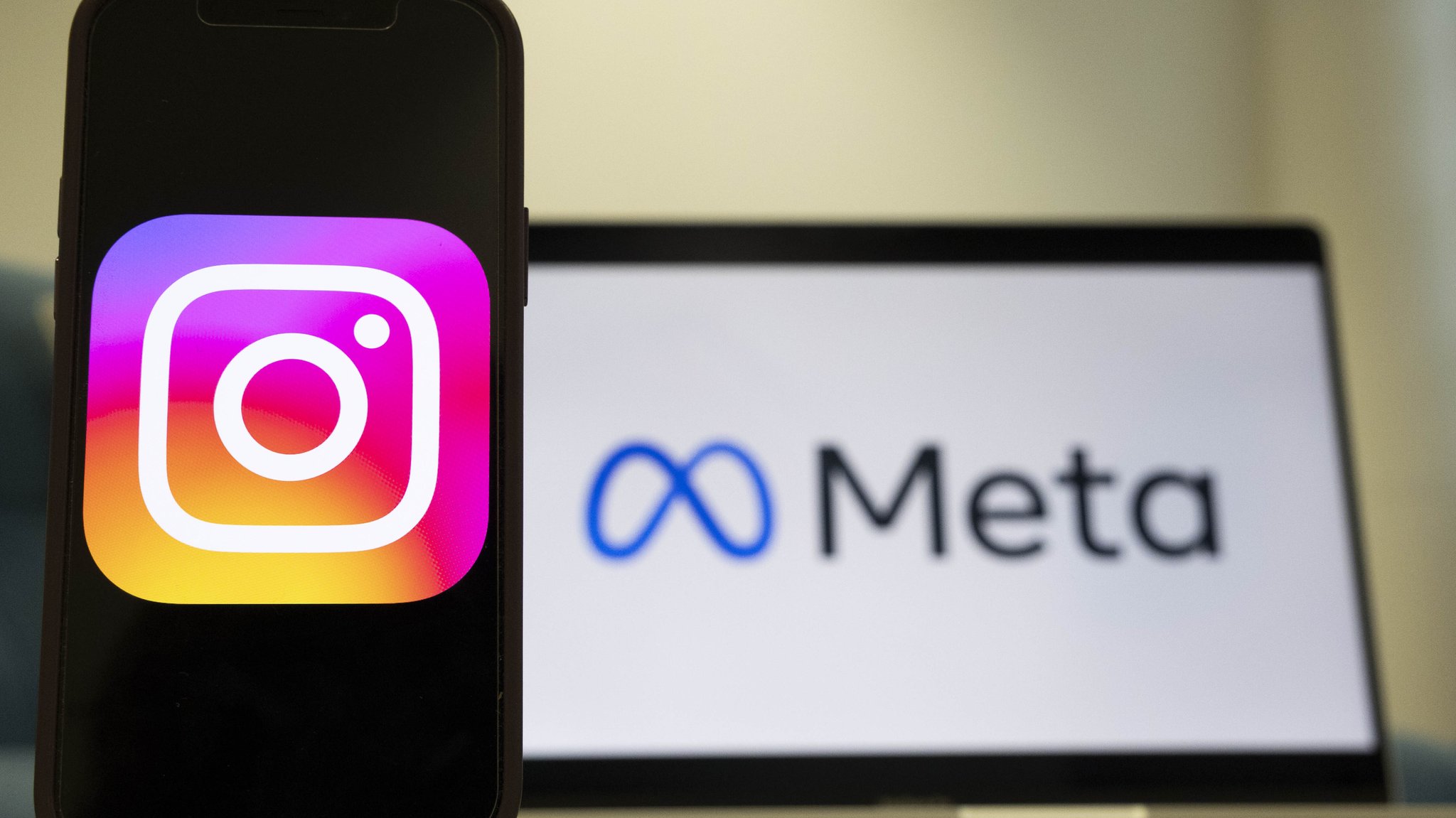 Instagram-Logo auf einem Smartphone, dahinter ein Laptop mit dem Meta-Logo.