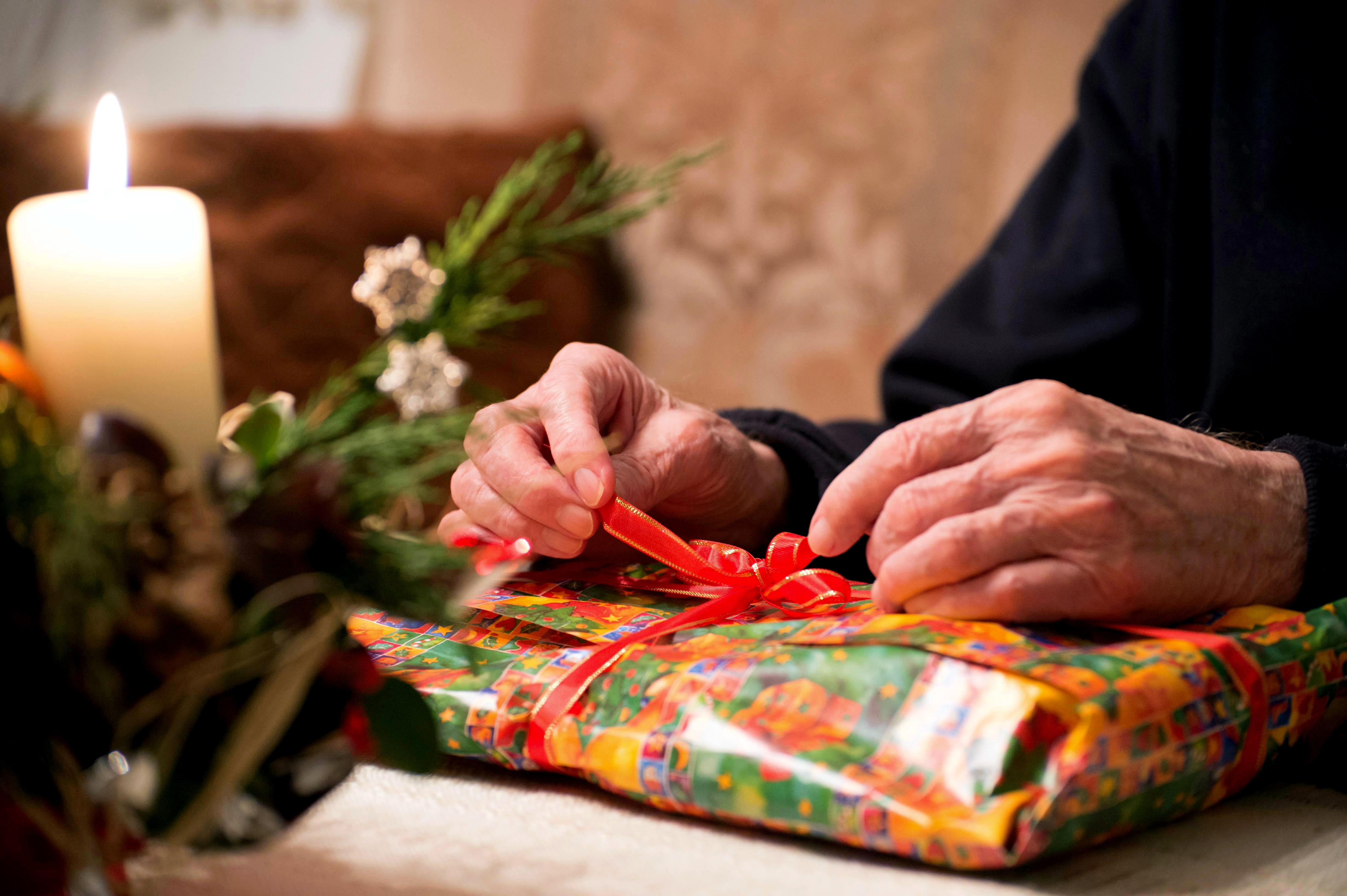 Ältere Hände binden die Schleife eines Weihnachtsgeschenks auf