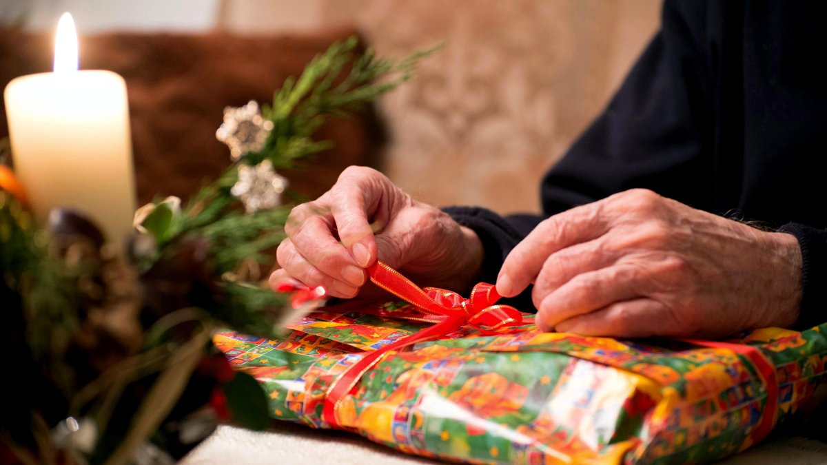 Ältere Hände binden die Schleife eines Weihnachtsgeschenks auf