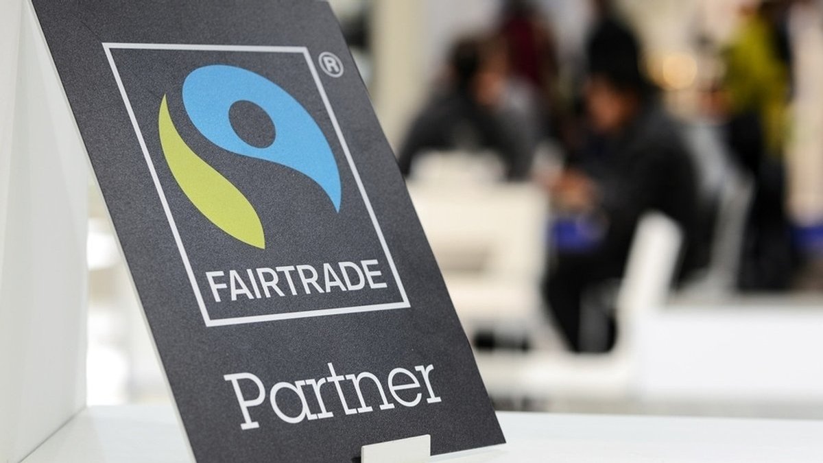 Auf einem schwarzen Schild ist das blau-grüne Logo "Fairtrade" zu sehen.