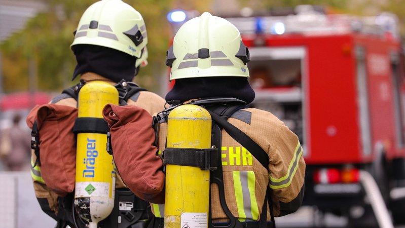 Symbolbild: Feuerwehrmänner mit Atemschutz, Helm und Druckluftflaschen von hinten am Einsatzort.