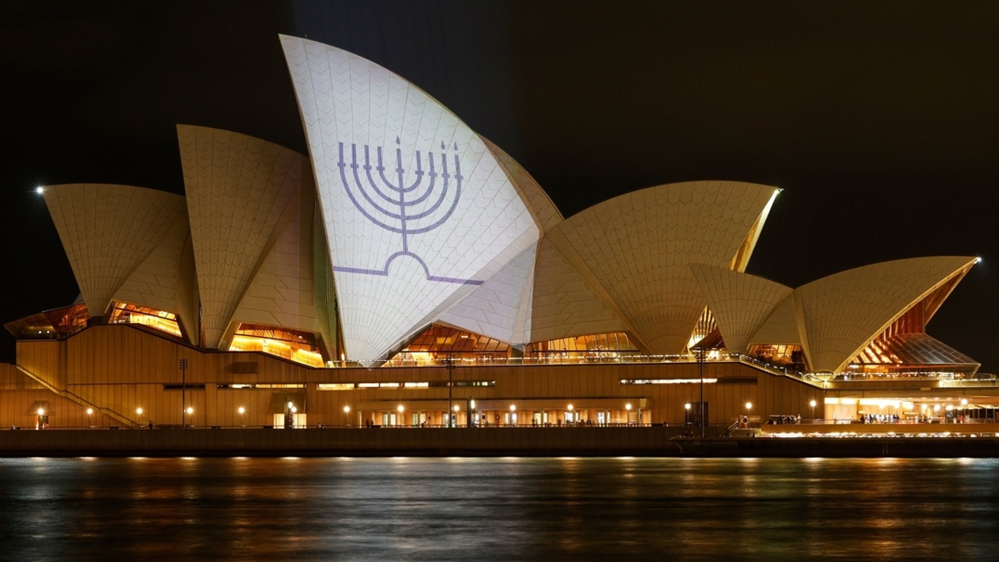 15.12.2025, Australien, Sydney: Die Segel des Opernhauses von Sydney sind in Gedenken an die Getöteten am Bondi Beach mit Kerzen auf einer Menora beleuchtet. 