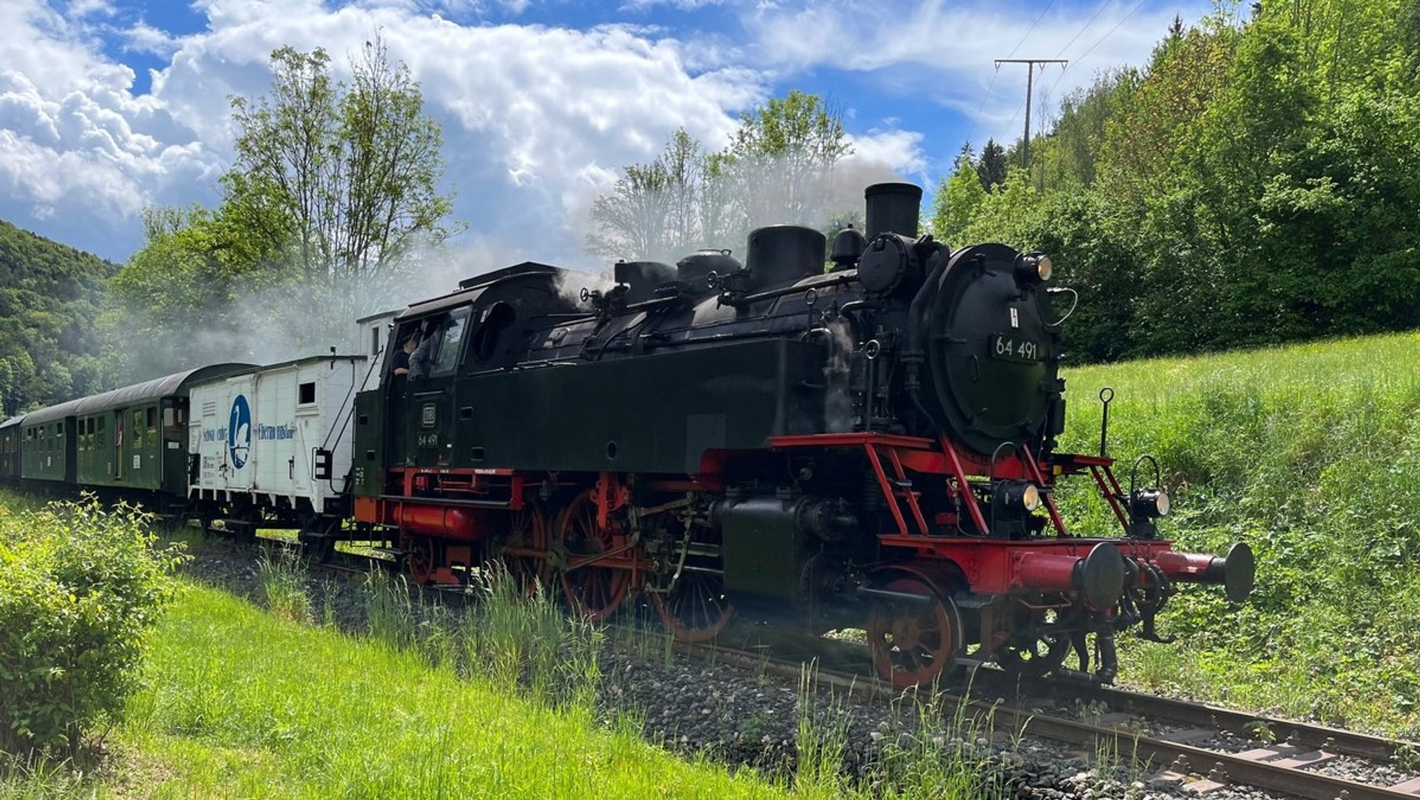 Eine Dampfbahn fährt durch ein grünes Tal. 