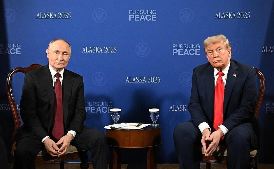 Die beiden Präsidenten Wladimir Putin und Donald Trump sitzen nebeneinander vor einer blauen Wand.