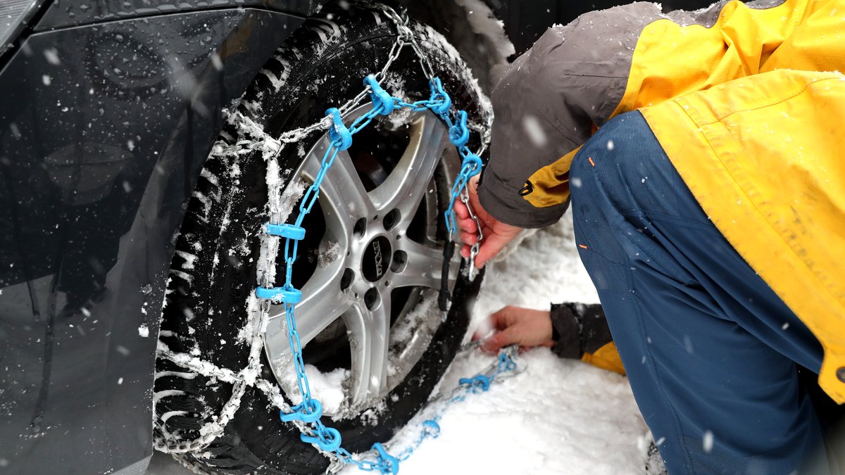 Ein Mann legt Schneeketten an den Reifen seines Autos an.