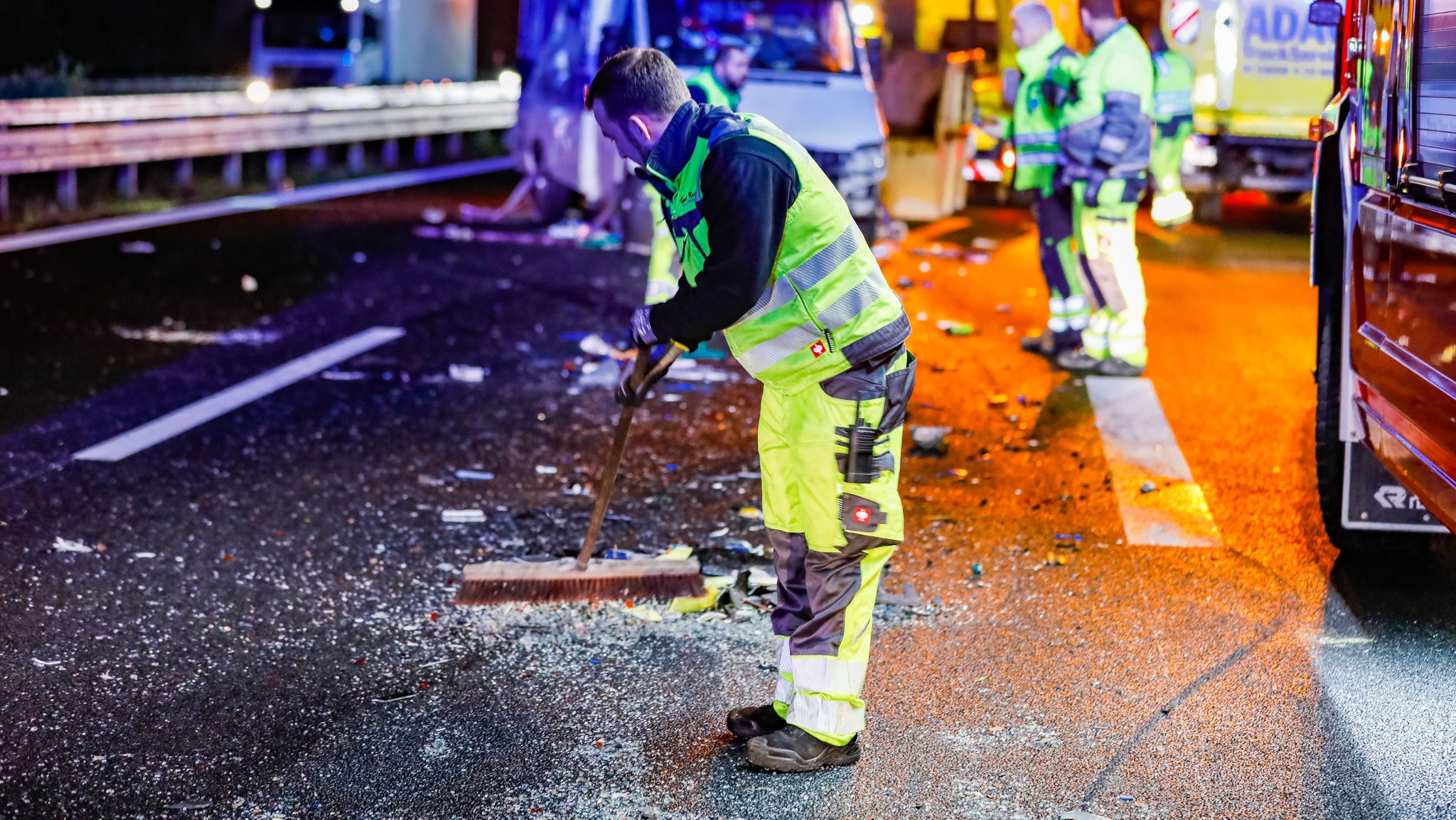 Ein Mann kehrt an der Unfallstelle die Fahrbahn, im Hintergrund Einsatzfahrzeuge und das Wohnmobil.