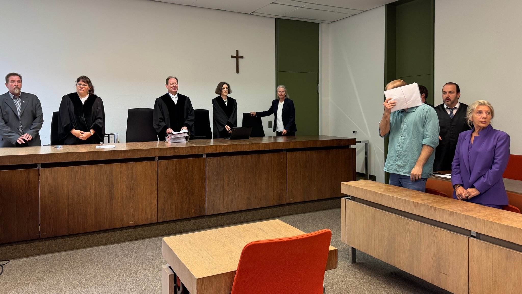 Zu sehen ist der Angeklagte, der sich Akten vor das Gesicht hält, seine Verteidigung und der Richter | Bild: BR/ Laura Goudkamp Zu sehen ist der Angeklagte, der sich Akten vor das Gesicht hält, seine Verteidigung und der Richter