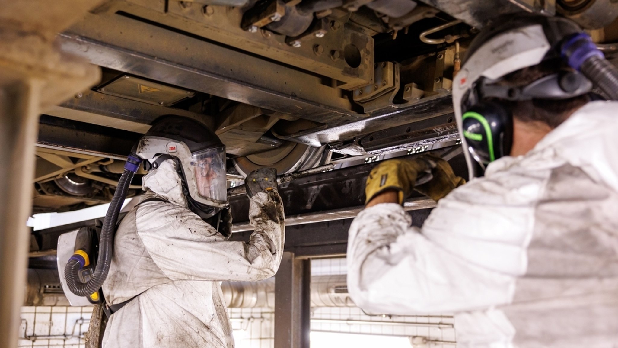 Mitarbeiter der Werkstatt der Verkehrsaktiengesellschaft VAG zeigen wie ein Trockeneisstrahlgerät angesetzt werden muss zur Reinigung eines durch Bitum verschmutzten Fahrwerks einer Straßenbahn.