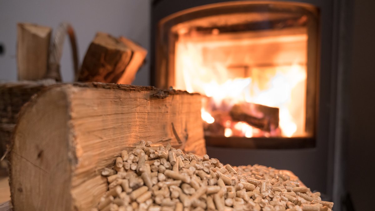 Ein Stück Holz und Holzbriketts liegen vor einem brennenden Ofen
