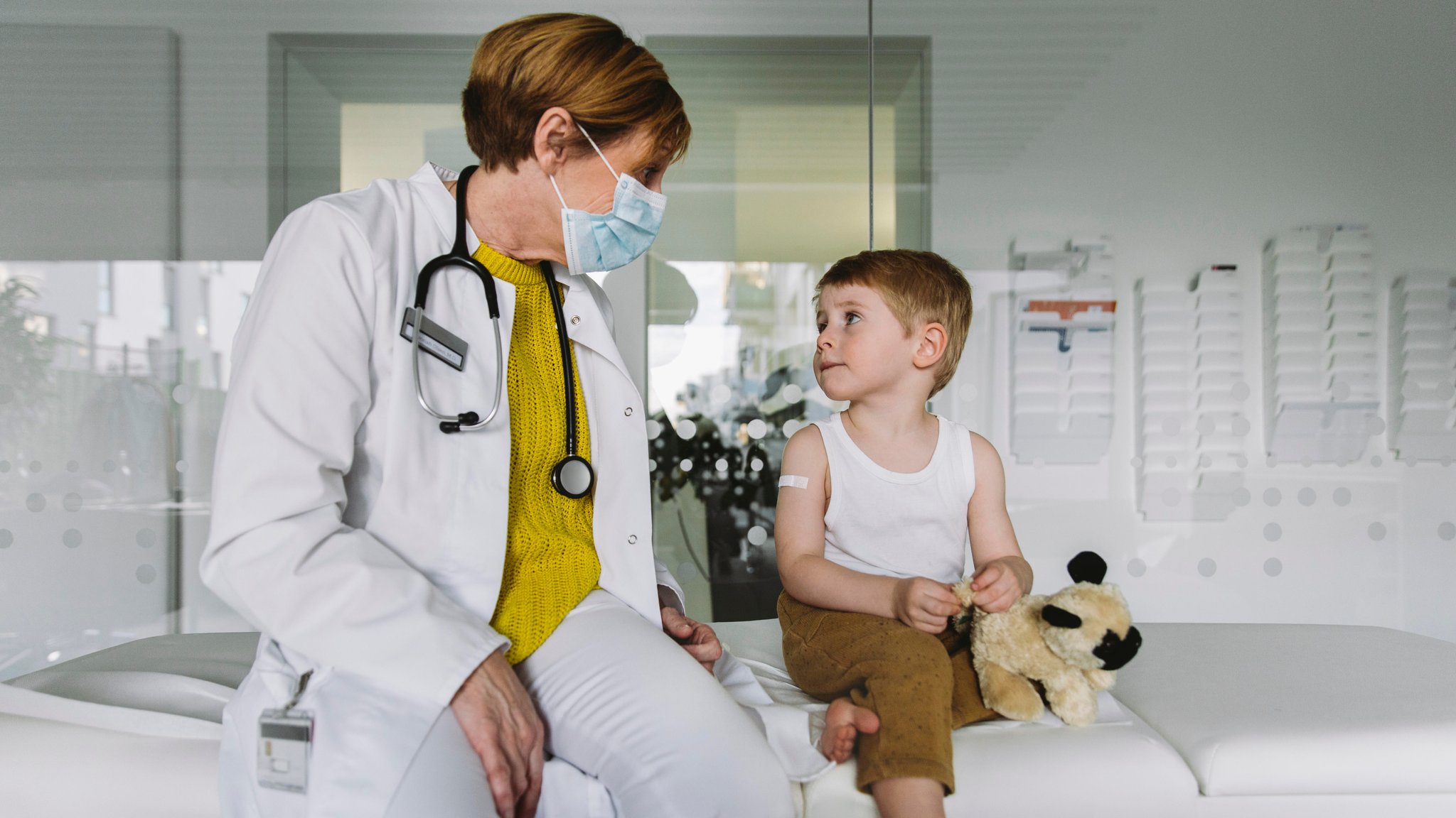 Eine Kinderärztin sitzt mit einem kleinen Patienten auf einer Liege eines Krankenzimmers.