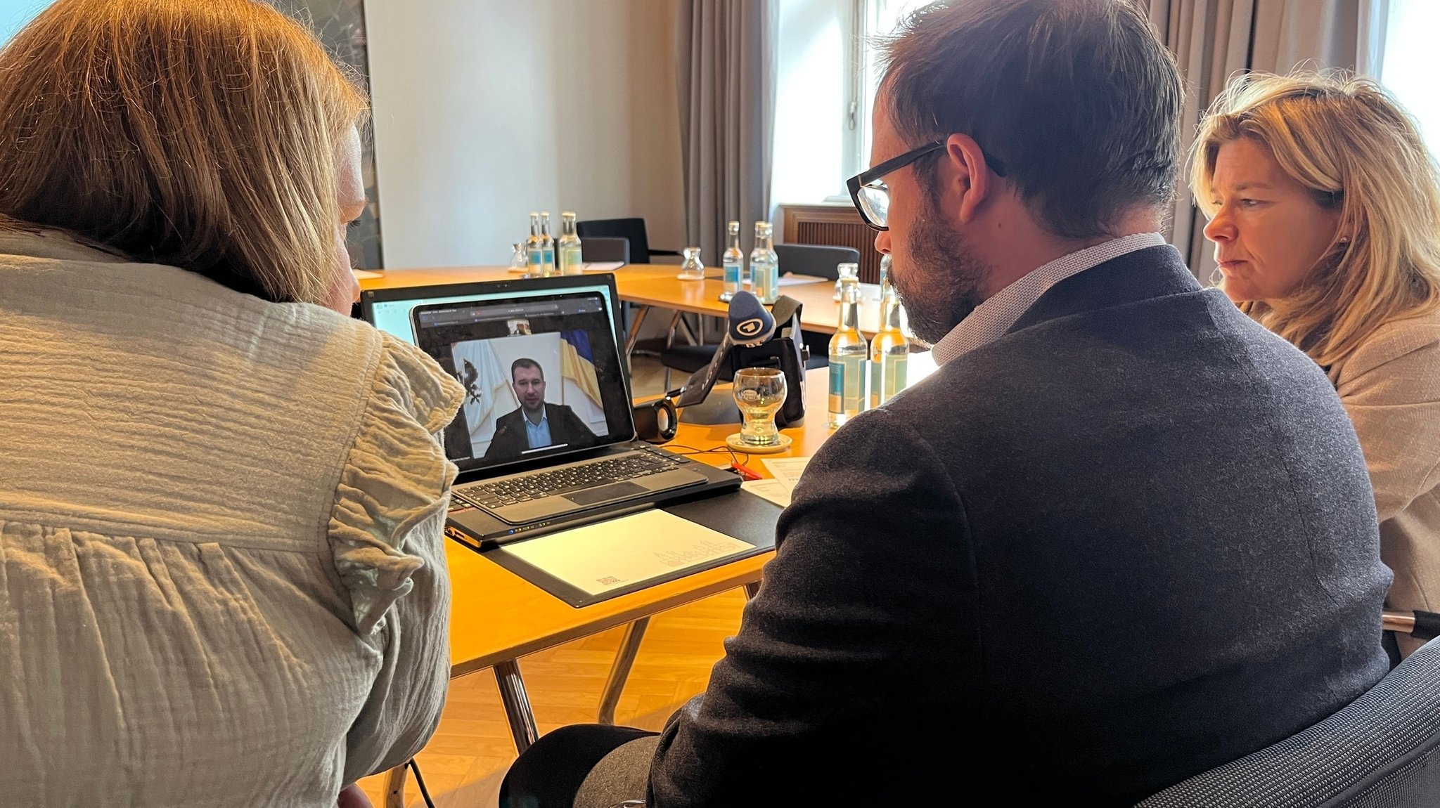 Der Memminger Oberbürgermeister Jan Rothenbacher, Partnerschaftsbeauftragte Alexandra Hartge und Übersetzerin Anna Kolomiiets sprechen vor einem Bildschirm in Tschernihiw mit dem Bürgermeister von Tschernihiw Oleksander Lomako.