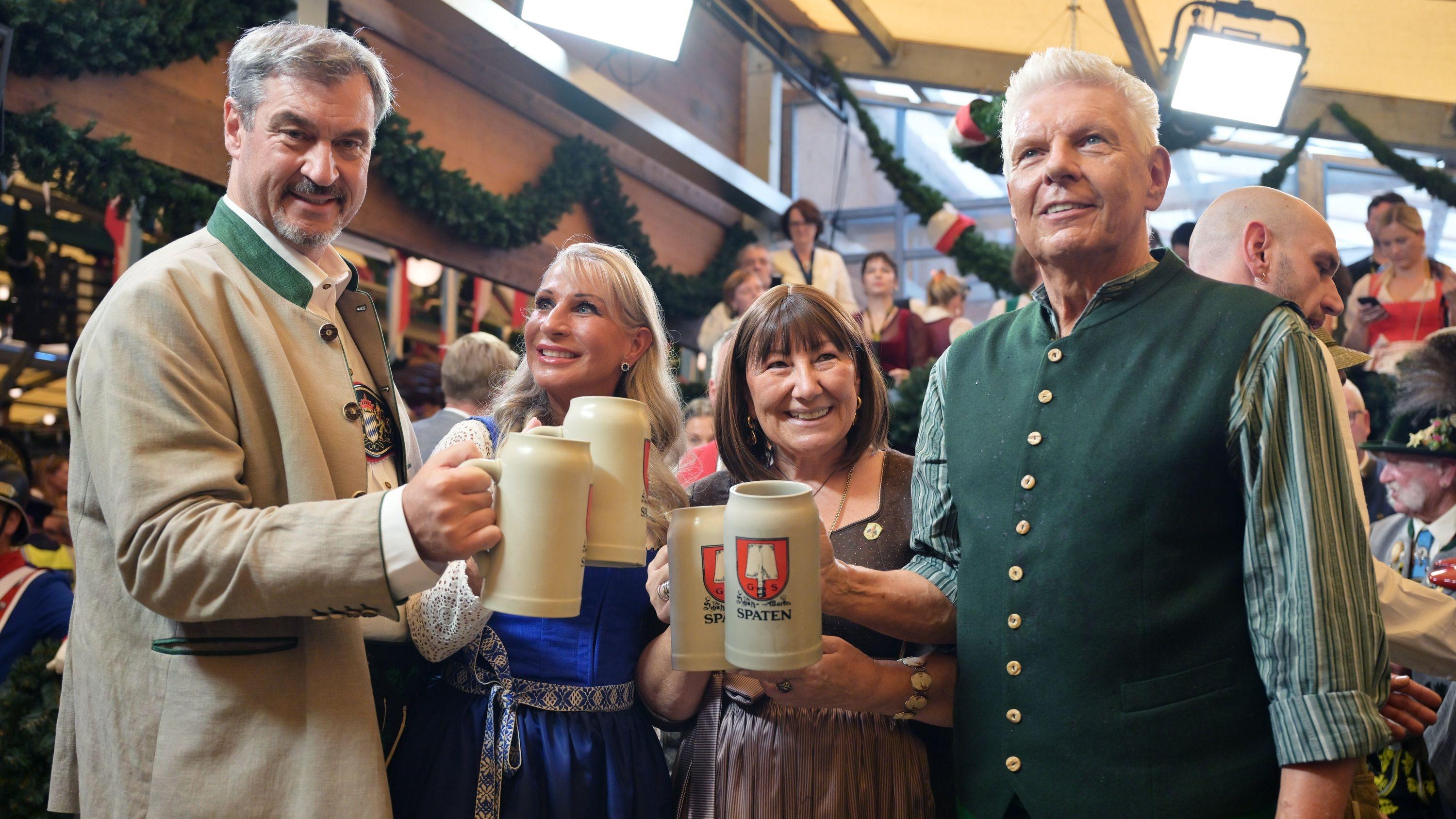 20.09.2025, Bayern, München: Markus Söder (CSU, l-r), Ministerpräsident von Bayern, mit seiner Frau Karin Baumüller-Söder, und Dieter Reiter (SPD, r), Oberbürgermeister von München, mit seiner Frau Petra, halten nach dem Anstich im Schottenhammel-Festzelt Bierkrüge. Die 190. Wiesn findet vom 20. September bis 05. Oktober 2025 auf der Münchner Theresienwiese statt. Foto: Peter Kneffel/dpa +++ dpa-Bildfunk +++