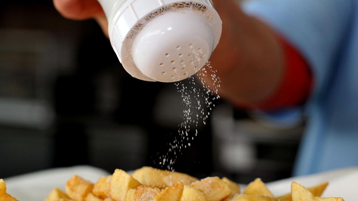  Salz wird mit einem Salzstreuer über Pommes Frites gestreut.
