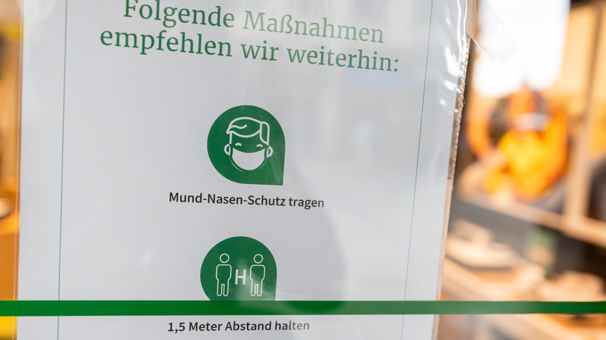 Ein Schild mit der Aufschrift "Folgende Maßnahmen empfehlen wir weiterhin: Mund-Nasen-Schutz tragen - 1,5 Meter Abstand halten" hängt am Eingang eines Geschäfts in der Innenstadt. 