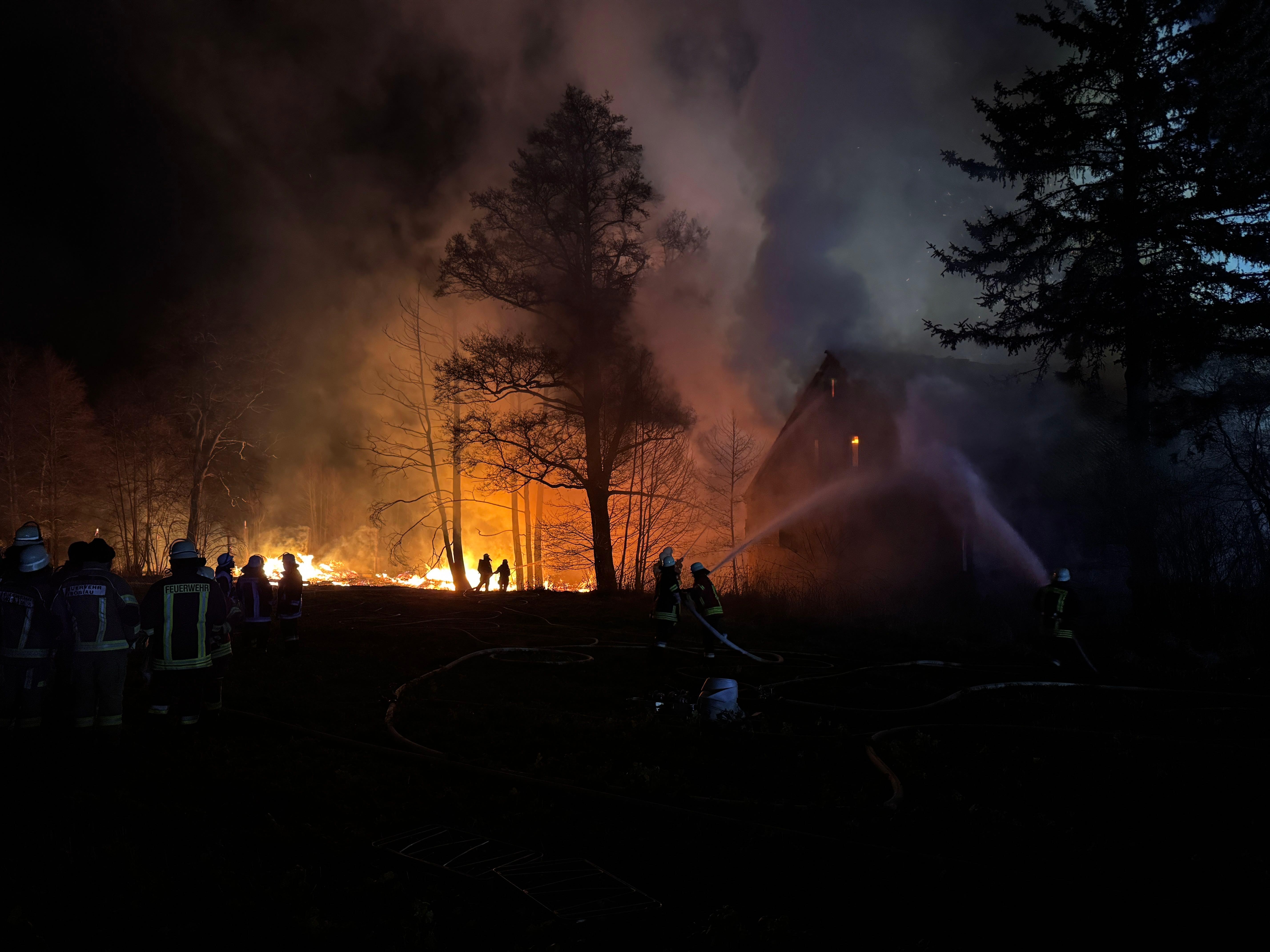 Flammen eines Feuers zeigen Feuerwehrkräfte bei Löscharbeiten an einem Gebäude.
