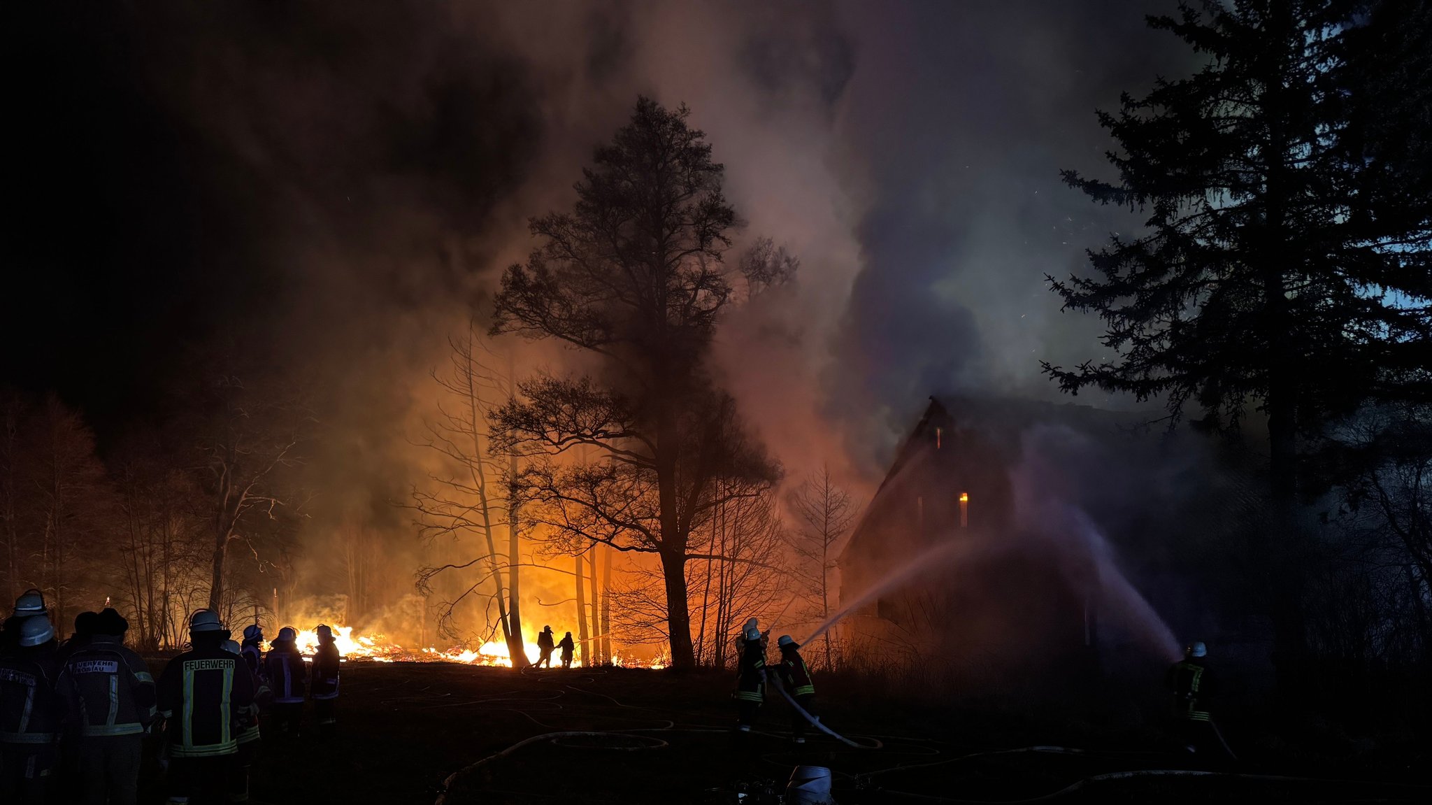 Flammen eines Feuers zeigen Feuerwehrkräfte bei Löscharbeiten an einem Gebäude.