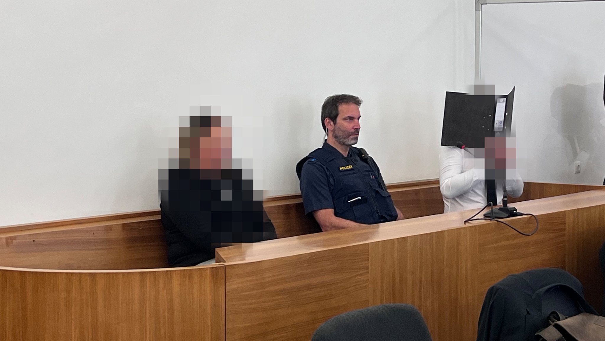 Das Ehepaar auf der Anklagebank, der Mann verbirgt sein Gesicht hinter einem Aktenordner.