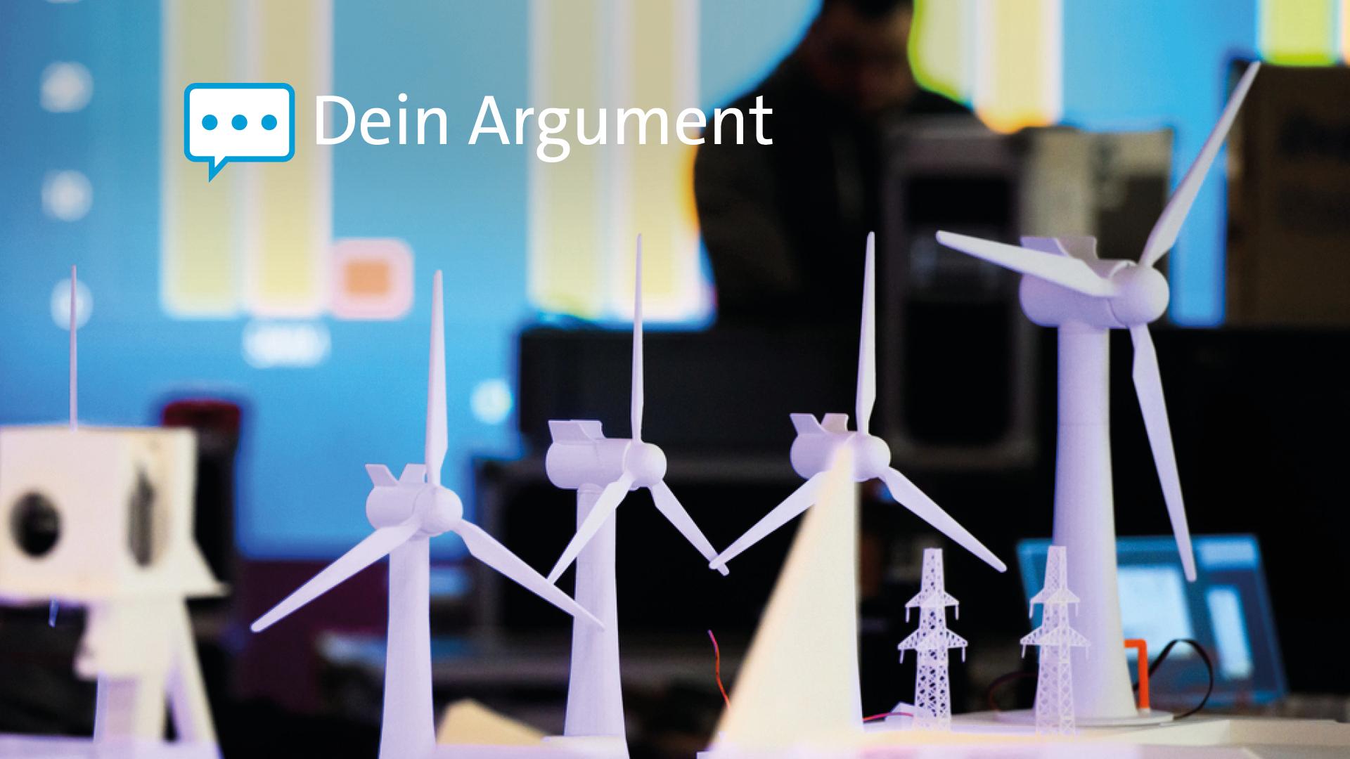 Kleine Modelle von Windrädern, im Hintergrund Menschen und Bilschirme auf einer Messe.