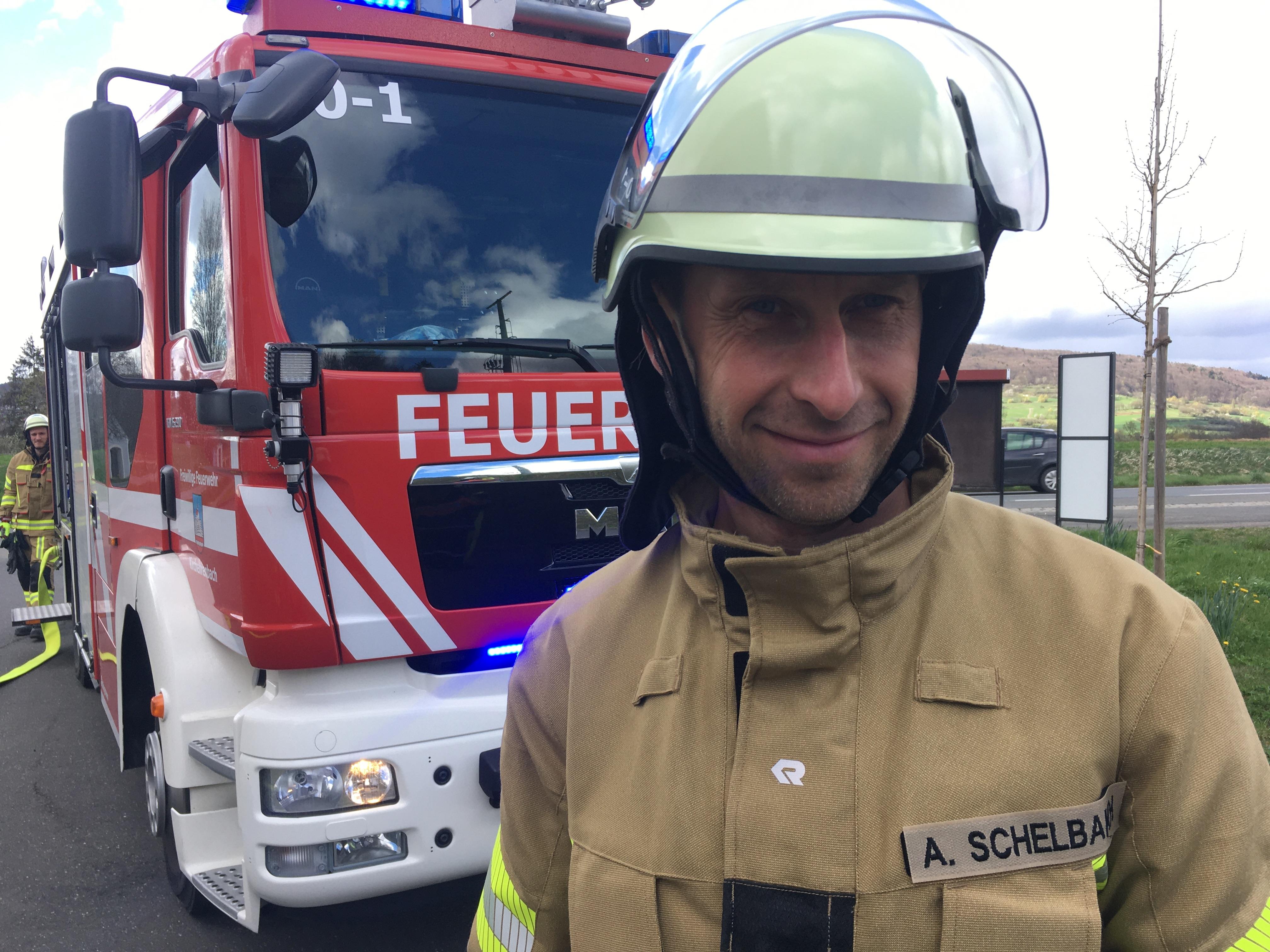 Alexey Shelbakh steht in Feuerwehrmontur vor einem Einsatzfahrzeug.