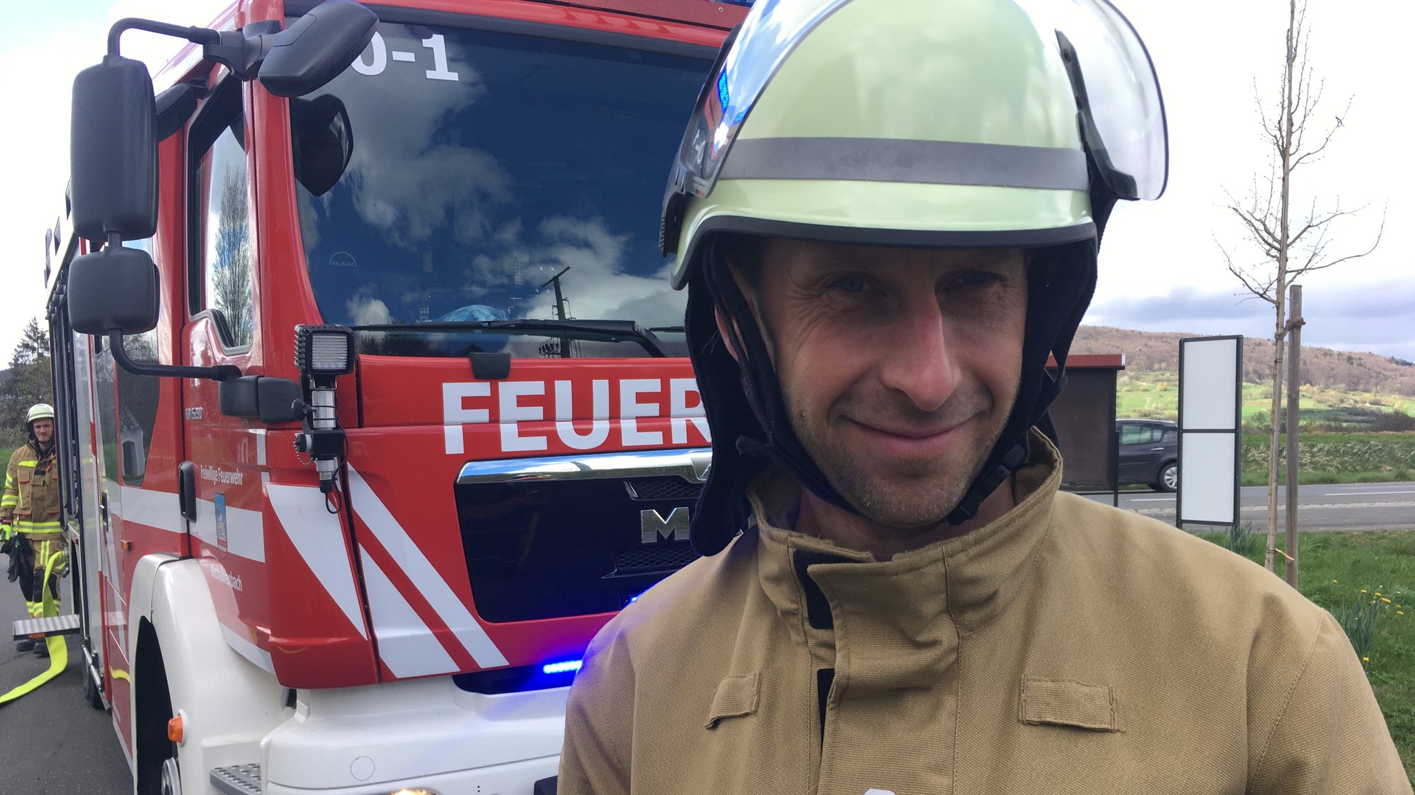 Alexey Shelbakh steht in Feuerwehrmontur vor einem Einsatzfahrzeug.