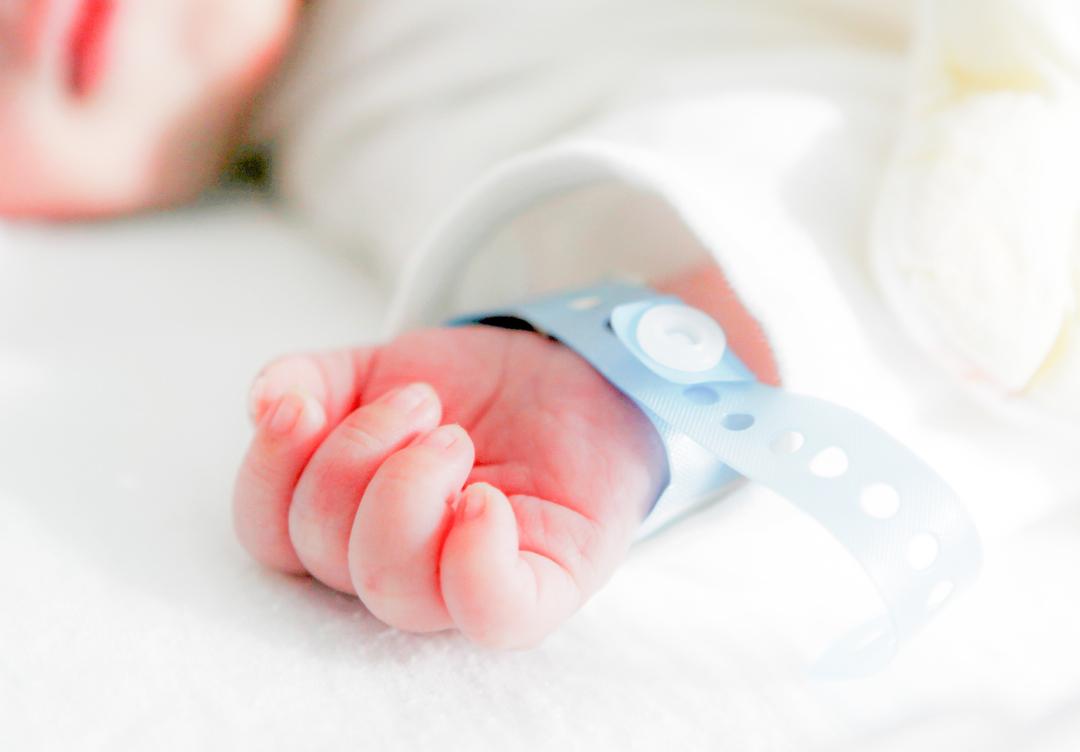 Symbolbild: Die Hand eines neugeborenen Babys mit Namensbändchen am Handgelenk.