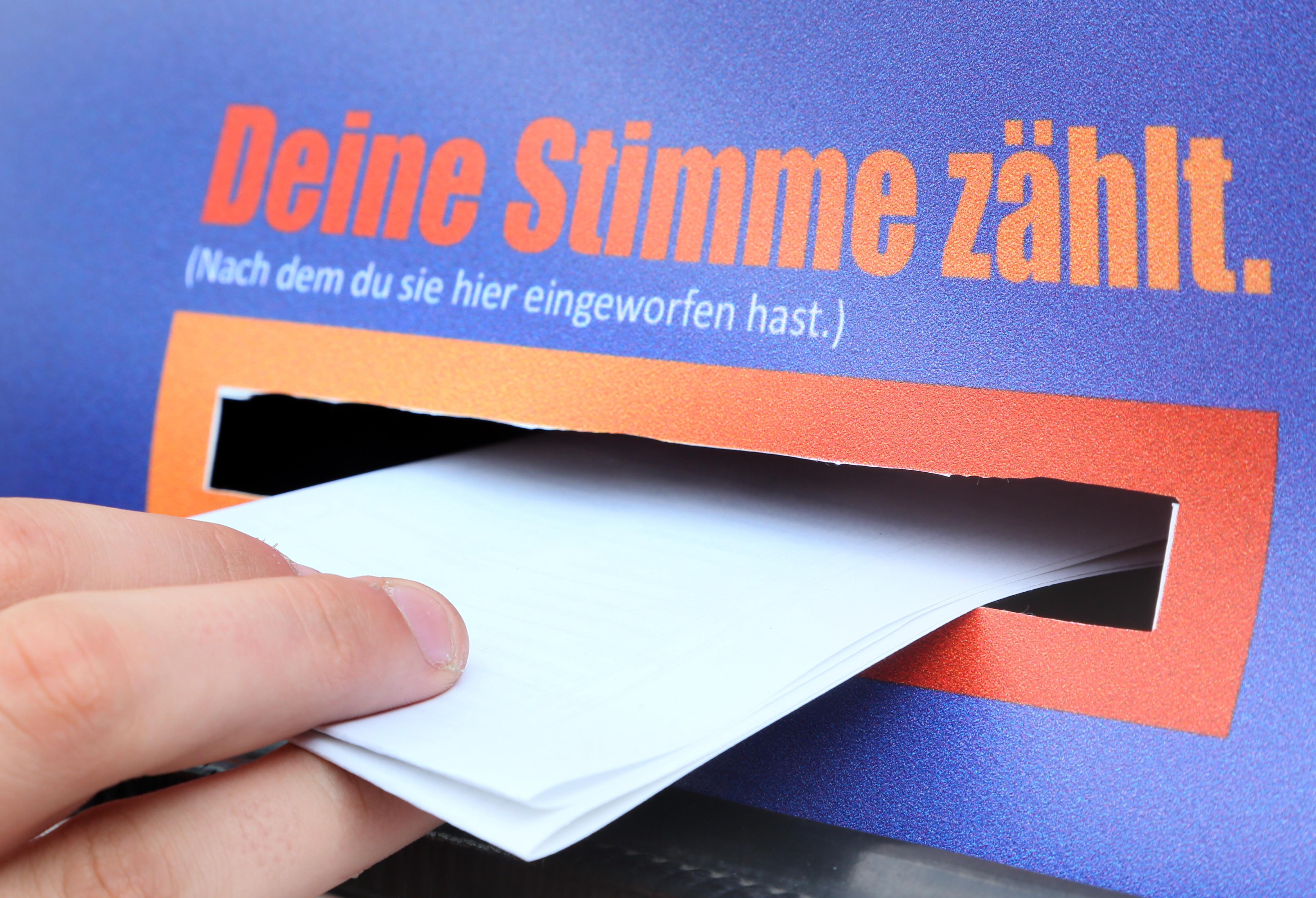 Eine Kinderhand wirft einen gefalteten Stimmzettel ein.