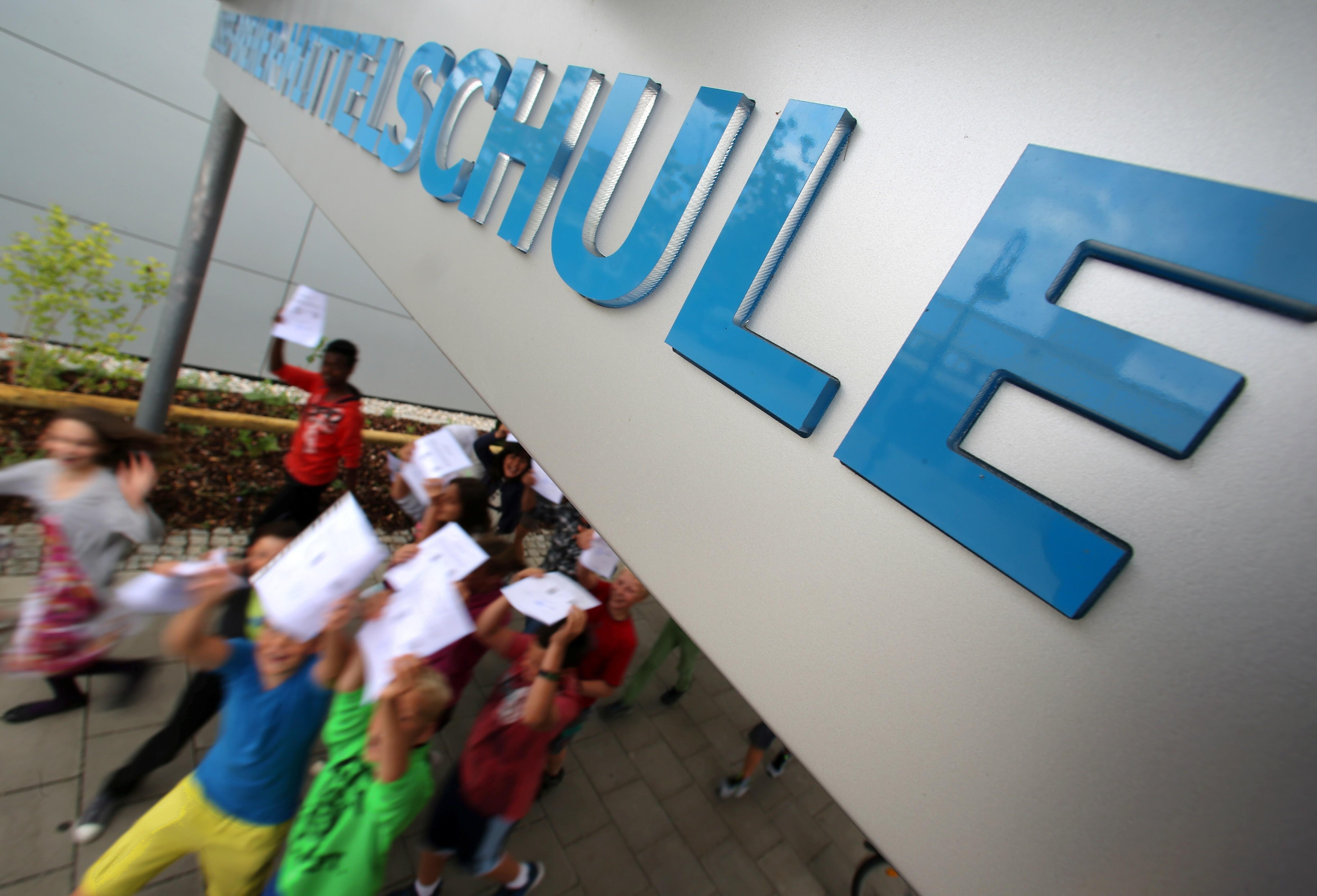 Schülerinnen und Schüler laufen mit ihren Zeugnisses aus der Schule