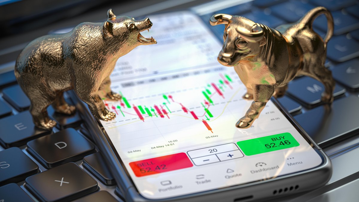 Figuren von goldenem Bär und goldenem Stier auf einem Smartphone, das Börsenkurse zeigt.