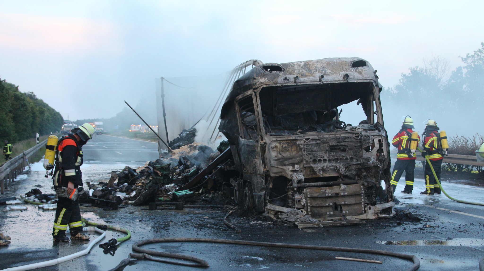 Feuerwehrleute neben einem ausgebrannten Lkw-Gerippe auf einer Autobahn.