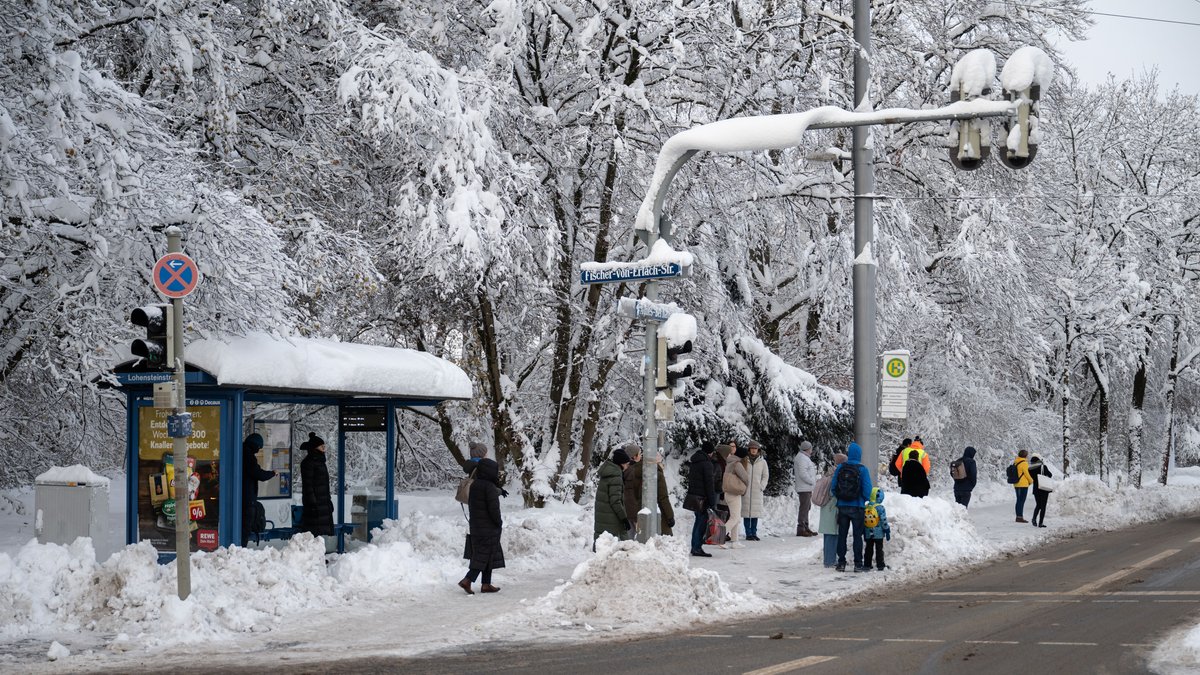 Fahrgäste warten am 4.12. an einer verschneiten Haltestelle in München auf einen Bus.
