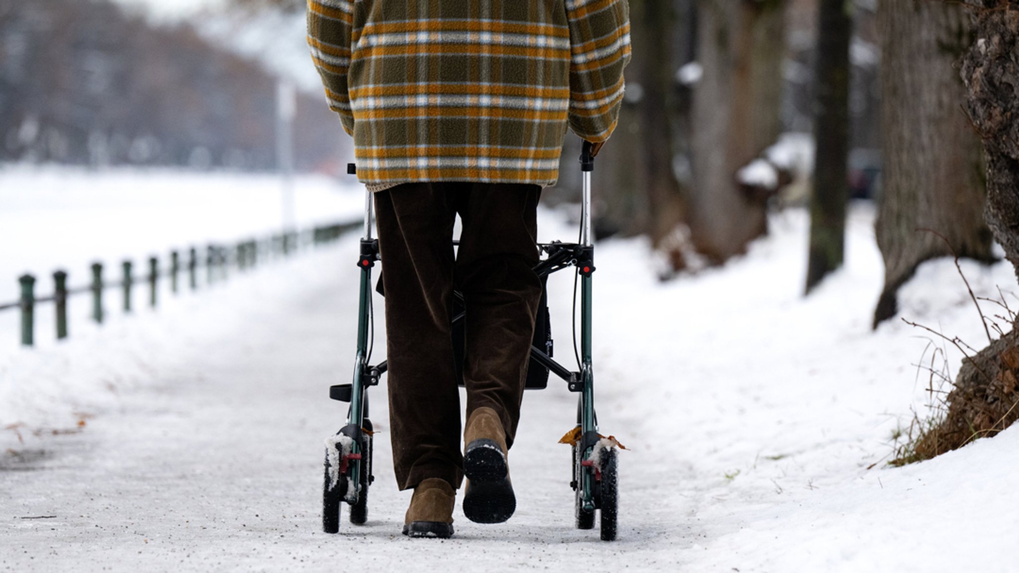 Ein Mann geht mit seinem Rollator am Nymphenburger Kanal über einen vereisten Gehweg. 